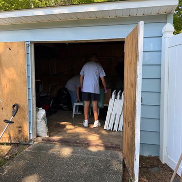 Two people organizing inside a shed with open doors.