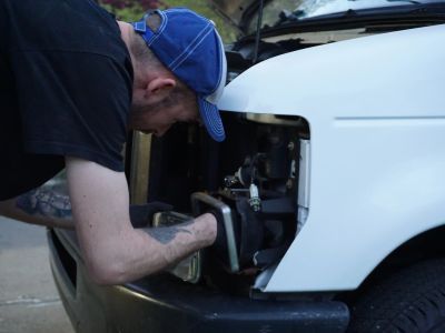Man repairing the front of a white vehicle outdoors.