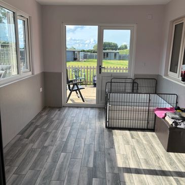 Bright sunroom with modern flooring and pet playpen near glass door.