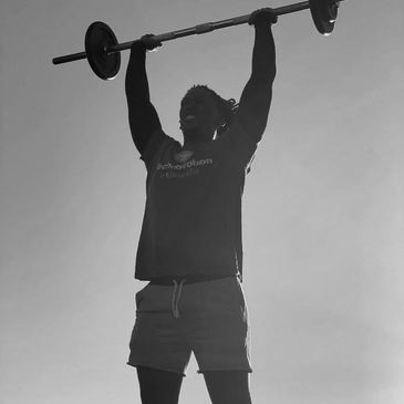 Man lifting a barbell overhead in black and white.