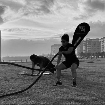 Two people exercising with battle ropes outdoors at sunset.