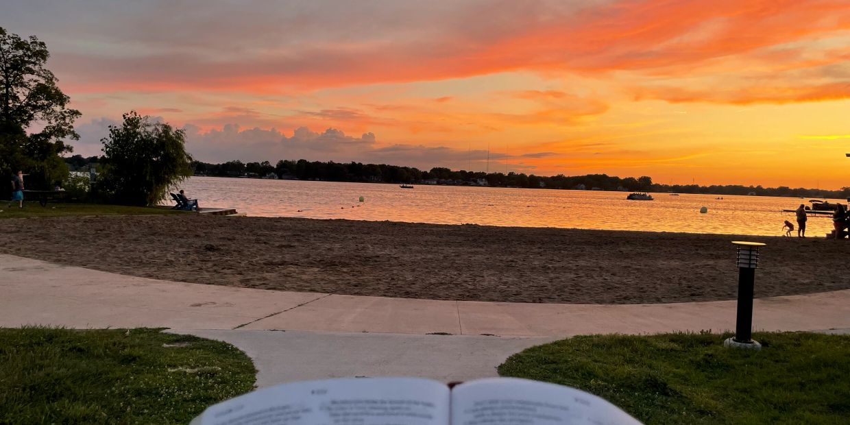 A serene sunset over a lake with a book in the foreground.