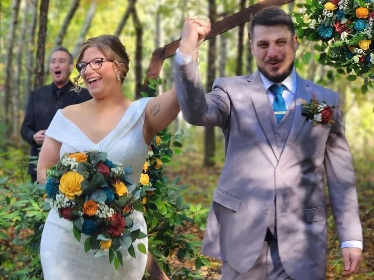 A happy wedding couple holding hands outdoors. The bride carries a fall-colored wood flower bouquet