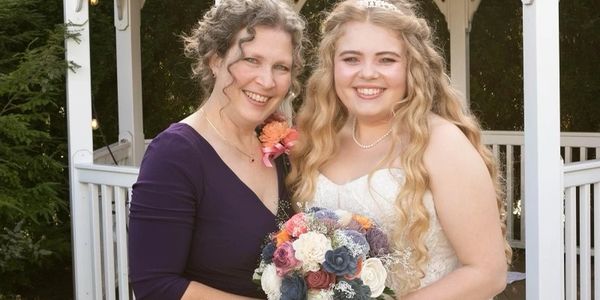 A mother and daughter at wedding holding wood flower bouquet in front of gazebo