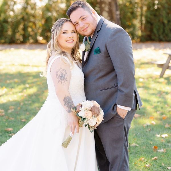 Bride in a long white dress holding a bouquet, smiling outdoors.

