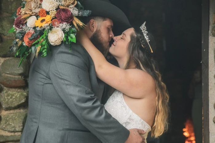 couple kissing, bride holds colorful bouquet of flowers. Photo credit: HeavenExposures Photography