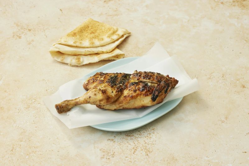 Charcoal chicken cooking over an open flame until the skin crisps