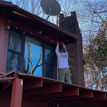 Man installing or repairing something above a window on a wooden deck roof.