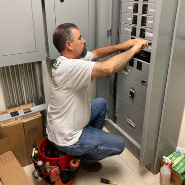 Electrician working on a circuit breaker panel in a utility room.