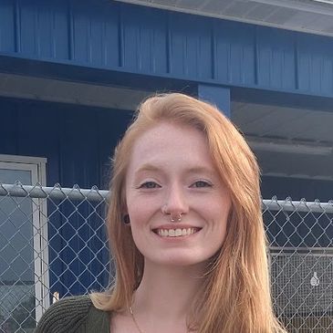 Smiling woman with long red hair wearing a green cardigan.