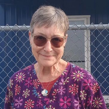 Smiling elderly woman in colorful snowflake-patterned scrubs and sunglasses.