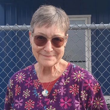 Smiling elderly woman in colorful snowflake-patterned scrubs and sunglasses.