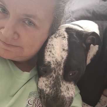 A woman snuggles closely with her black and white dog, sharing a quiet moment.