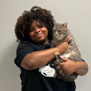 Woman smiling while holding a gray cat against a plain background.