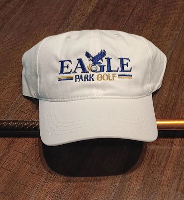 White golf cap with embroidered "Eagle Park Golf" logo on wooden surface.