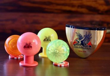 Colorful golf ball markers and a USA Park Golf club head on a wooden surface.