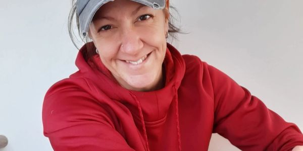Femme souriante en sweat rouge et casquette grise.