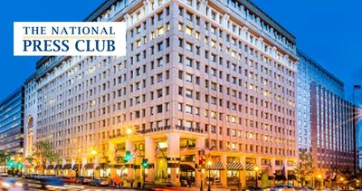 The National Press Club building illuminated at dusk in a bustling city area.