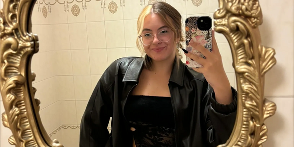 Young woman taking a mirror selfie in a bathroom wearing glasses and a black outfit.