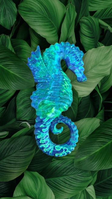 A vibrant blue and green seahorse sculpture on lush green leaves.