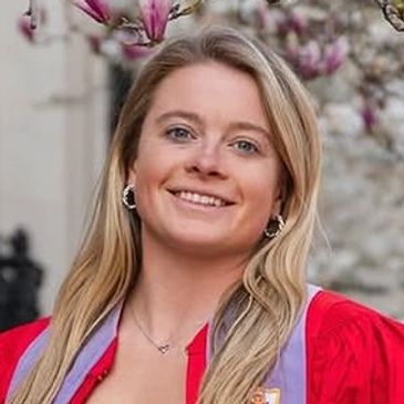 A smiling woman in a red graduation gown with flowers in the background.