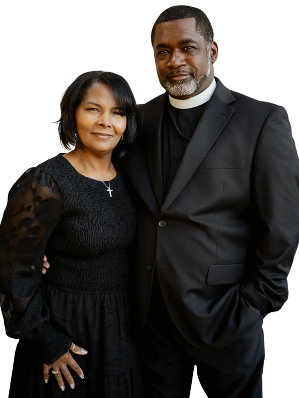 A couple dressed in black, the man in clergy attire, the woman wearing a cross necklace.