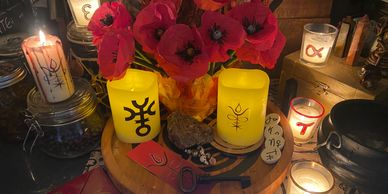A mystical altar with candles, red flowers, and symbolic objects arranged on a wooden tray.
