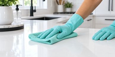 Person cleaning a kitchen counter with gloves and cloth.