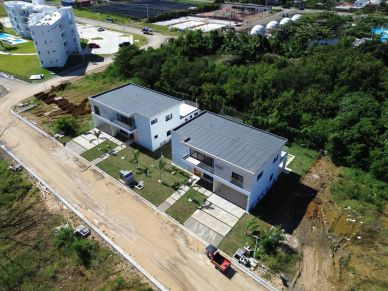 Aerial view of two modern white houses with flat roofs surrounded by greenery.