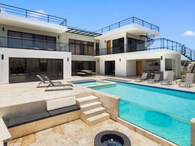 Modern two-story house with pool and outdoor seating area under clear sky.
