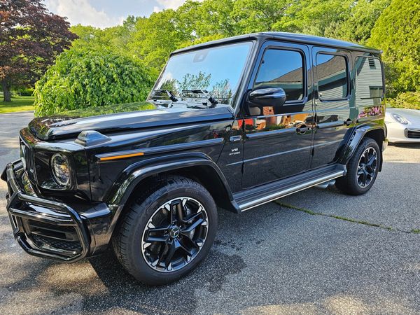 Black Mercedes-Benz G-Class SUV parked on driveway with lush greenery.