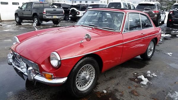 Classic red vintage car parked on a wet street with snow patches.