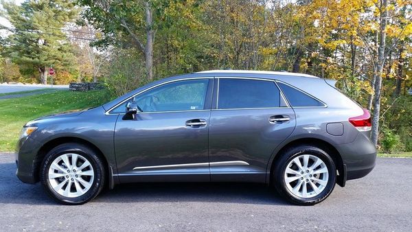 Gray SUV parked on a paved road beside a green and autumn tree landscape.