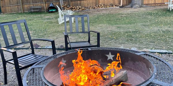 Outdoor fire pit with chairs arranged around it in a backyard.