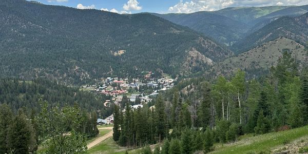 A small town nestled in a lush mountain valley under a partly cloudy sky.