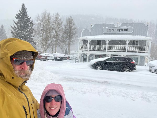 Two people in winter clothes posing in front of Hotel Ryland in snowy weather.