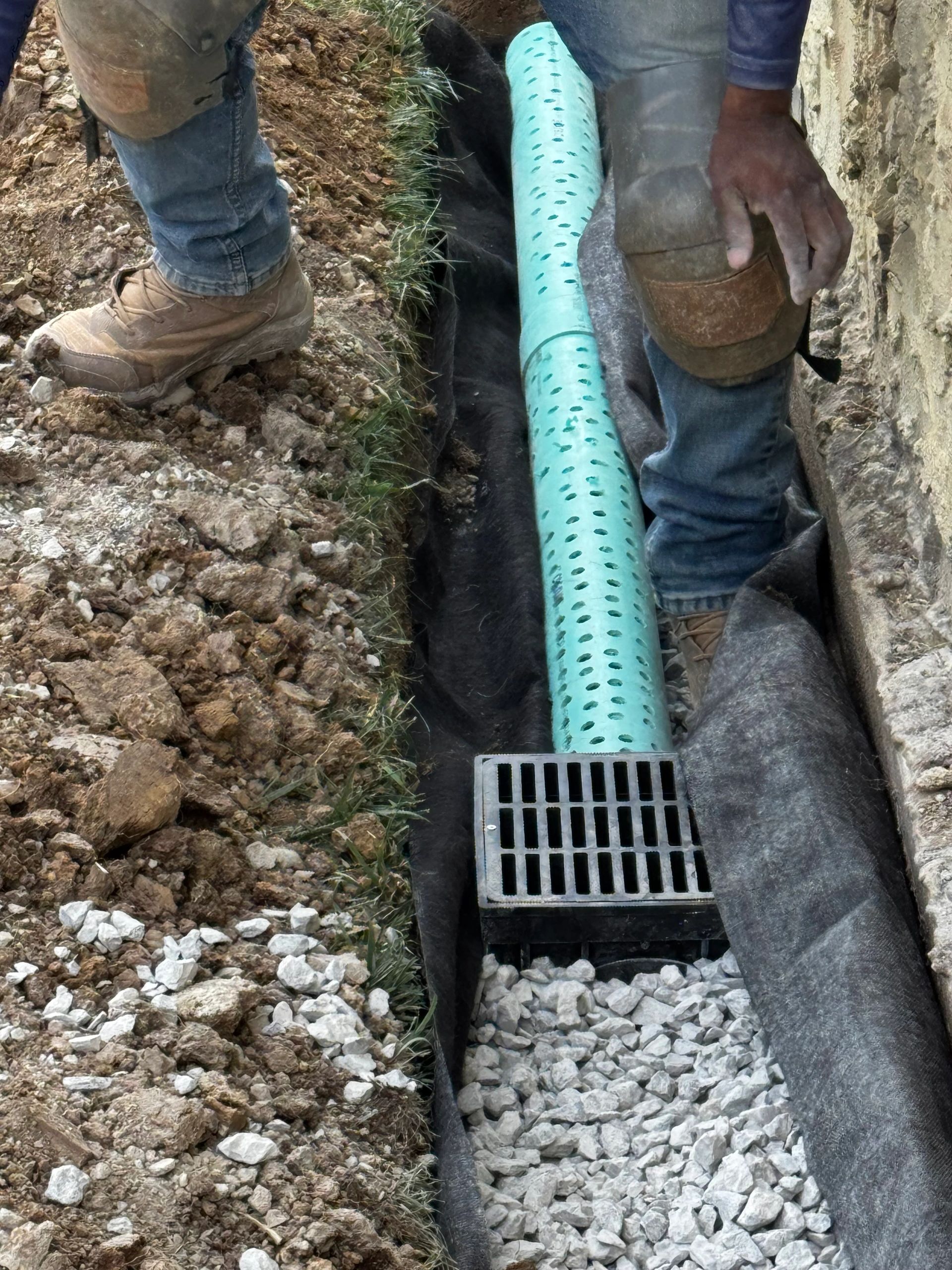 Worker installing a drainage system with gravel and perforated pipe.