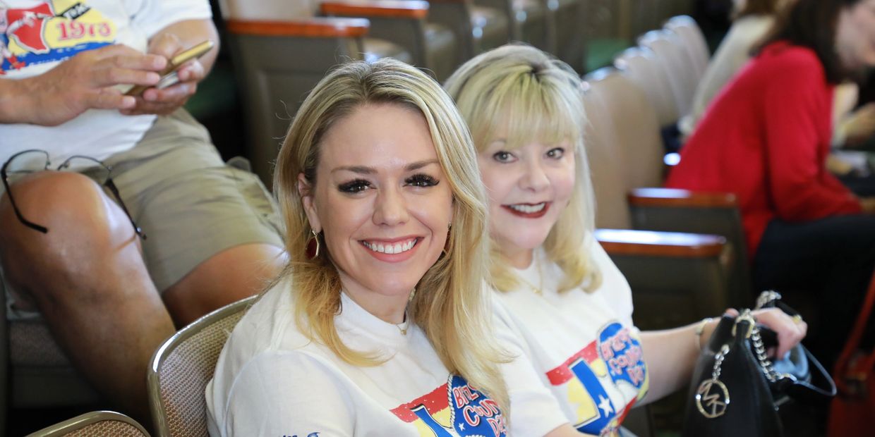 Two smiling women wearing matching event t-shirts seated indoors.
