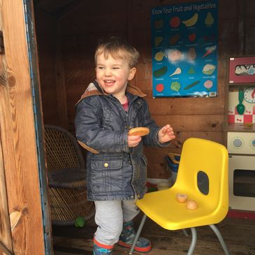 A child in a wendy house in outdoor space at Avening playgroup