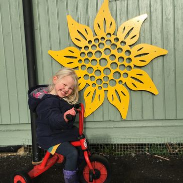 A child on tricycle in front of a sunflower logo.