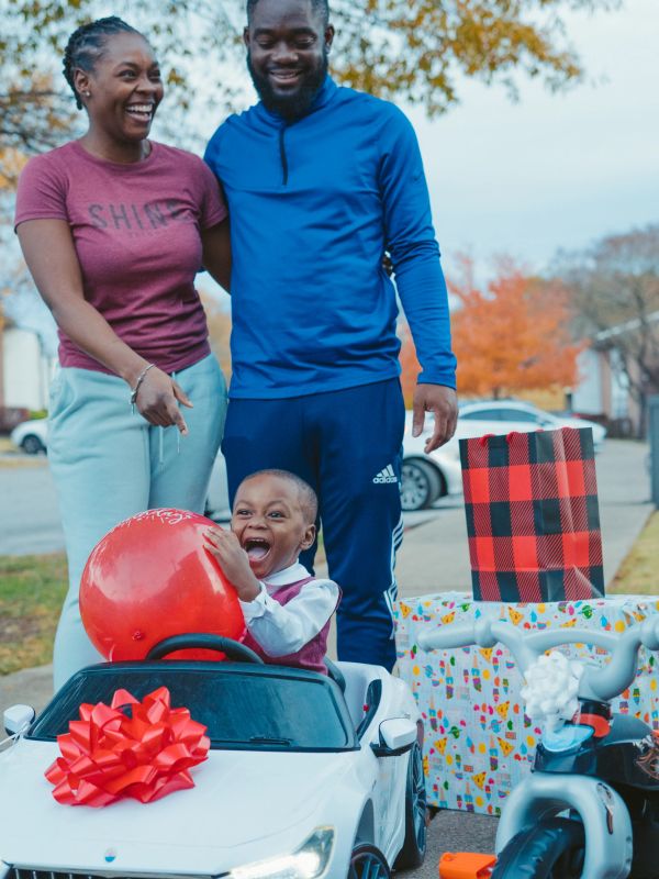 Happy child in toy car with parents and gifts.