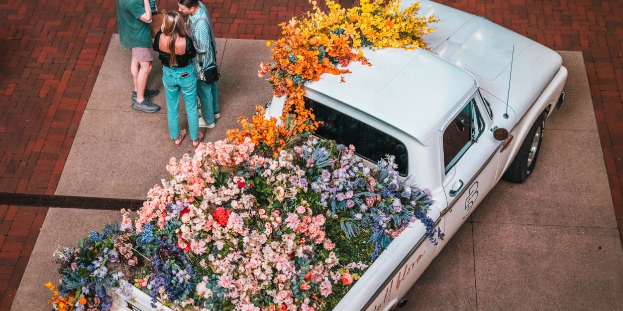 White truck filled with colorful flowers and three people standing nearby.