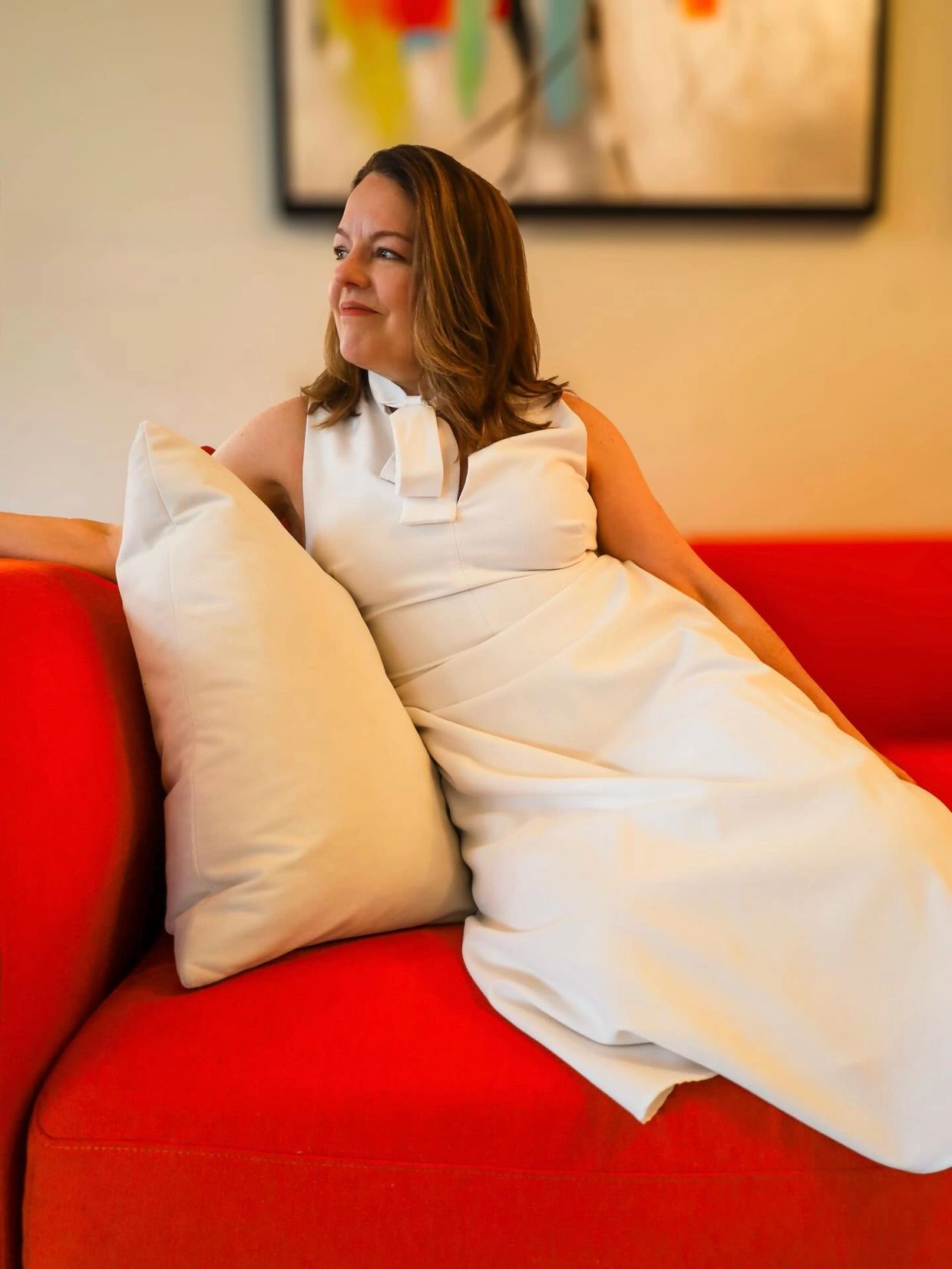 Woman in white dress reclining on a bright red couch with a white pillow.