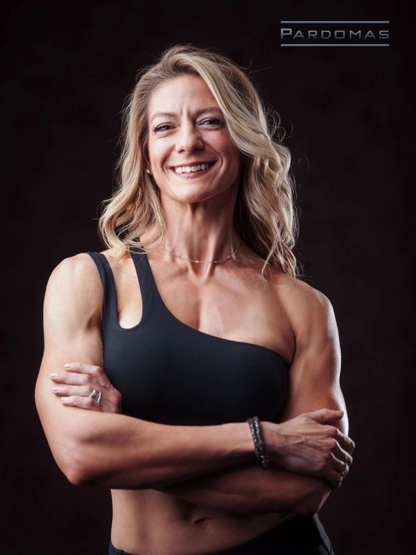 White woman with blonde hair, arms crossed, wearing black sports bra and black leggings. 
