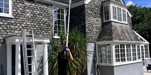 Person using a tool on a house wall near a ladder.