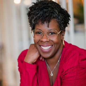 Professional headshot of Black Woman wearing glasses smiling for camera. 