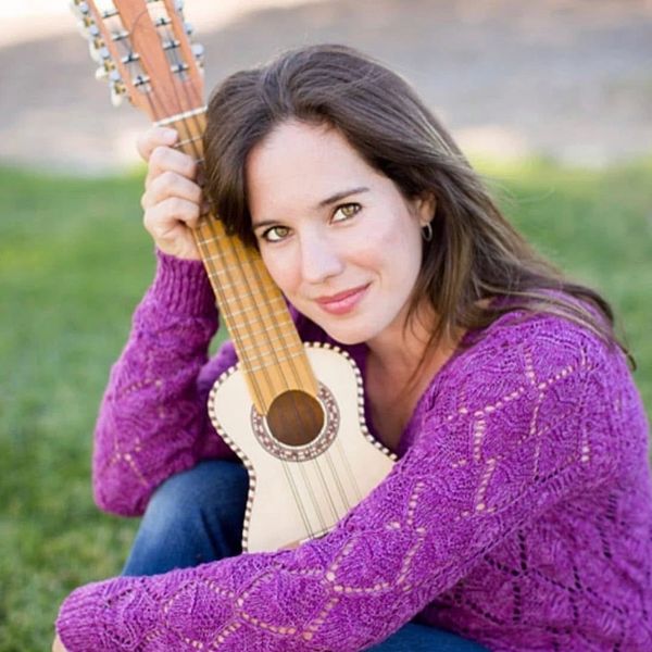 Woman in purple sweater holding a small guitar outdoors.