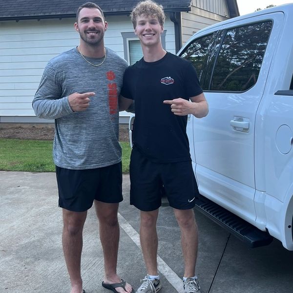 Two young men smiling and pointing at each other outdoors.