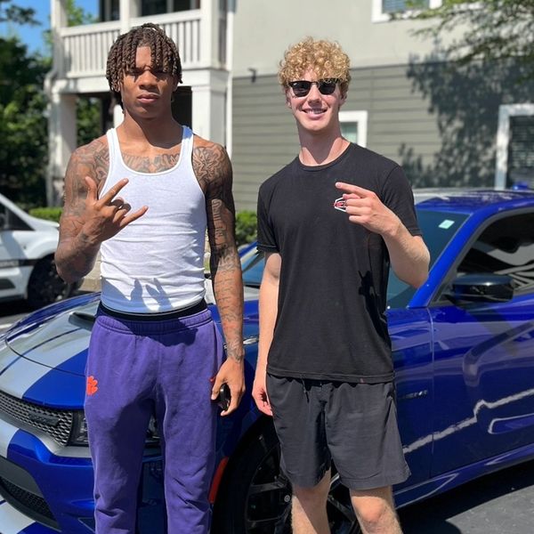 Two young men posing by a blue sports car.
