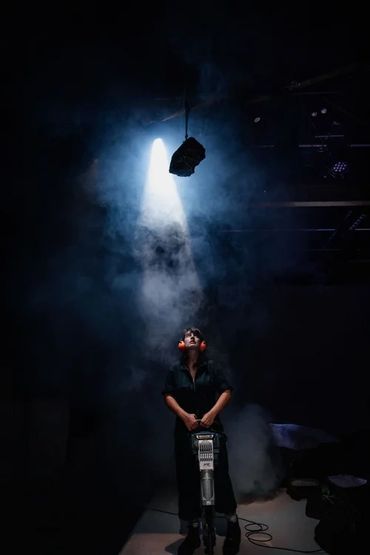 Person in dark room with spotlight and safety earmuffs.